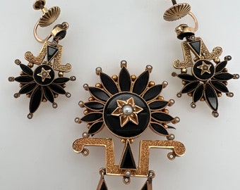 May include: A gold tone brooch and matching earrings with black enamel and pearl accents. The brooch features a starburst design with a central star and three dangling triangles.