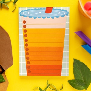 May include: A yellow and orange to-do list notepad with a cartoon illustration of a boba tea cup with a straw. The notepad has a grid pattern and a white border.