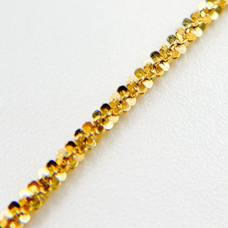 May include: A gold chain necklace with a delicate, textured design. The chain is made up of small, linked squares.