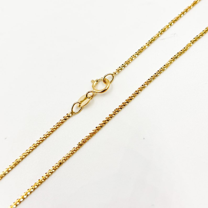May include: A gold chain necklace with a lobster clasp closure. The chain is a delicate, fine-link style.