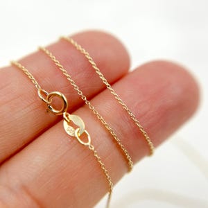 May include: A delicate gold chain necklace with a small clasp. The chain is thin and appears to be made of small, connected links. The necklace is a bright, shiny gold color and is displayed against a light background.
