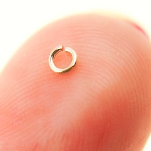 May include: A small, gold-colored jump ring, a type of jewelry finding used for connecting chains, cords, or other jewelry components.