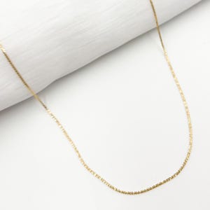 May include: A delicate gold chain necklace with a fine, textured design. The chain is thin and has a subtle shimmer.