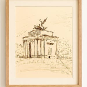May include: Pen and ink sketch of a monument with a chariot and winged figure on top, set against a light background. The artwork is framed in a light wood frame, showcasing the architectural details.