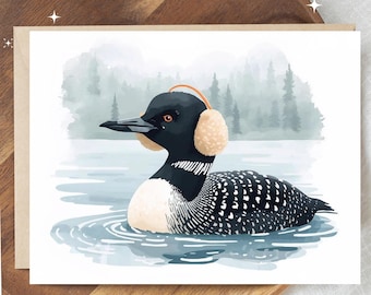 May include: A greeting card featuring a watercolor illustration of a loon wearing earmuffs, floating on a lake. The loon has black and white feathers, a black beak, and orange eyes. The background shows a misty forest.