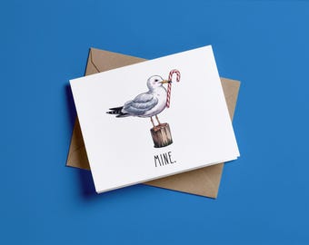 May include: A white greeting card featuring a gray and white seagull standing on a wooden post, holding a red and white striped candy cane in its beak. The word MINE is printed in black capital letters below the illustration.