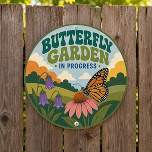 May include: A circular sign featuring the text BUTTERFLY GARDEN IN PROGRESS in dark green and blue letters. The illustration depicts a monarch butterfly perched on a pink coneflower, with purple bell-shaped flowers, green hills, and orange clouds.