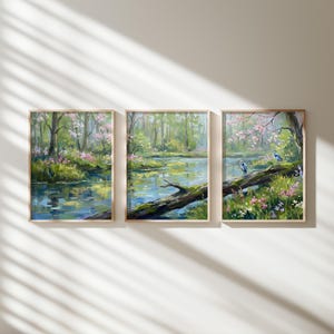 May include: Set of three framed landscape paintings. Each features a serene waterscape with trees, pink blossoms, and reflections. The artwork evokes a sense of tranquility with its soft colors and natural elements.