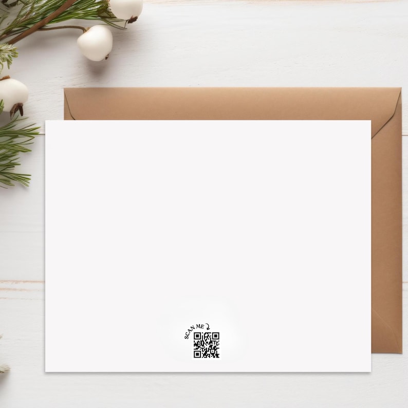 May include: A white greeting card with a brown envelope. The card has a QR code in the lower right corner with the text "SCAN ME?". The card is on a white wooden surface with greenery and white berries in the upper left corner.