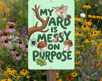 May include: A light green metal sign with the text "MY YARD IS MESSY ON PURPOSE" in a playful font. The sign features illustrations of a hummingbird, ladybug, spider, mushrooms, and a worm. It is mounted on a wooden post and surrounded by flowers.