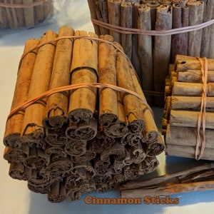 May include: A close-up of a bundle of cinnamon sticks tied together with rubber bands. The sticks are arranged in a spiral pattern and are a rich brown color. The text "Cinnamon Sticks" is visible at the bottom of the image.