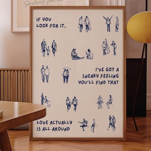 May include: A framed print with a wooden frame featuring blue illustrations of people and the text "IF YOU LOOK FOR IT" and "LOVE ACTUALLY IS ALL AROUND". A postcard with the text "Sending you all" is also visible.