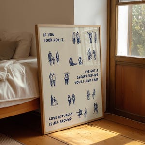 May include: A framed art print with a light wood frame. The print features blue line drawings of people in various poses and the phrases "IF YOU LOOK FOR IT," "I'VE GOT A SNEAKY FEELING YOU'LL FIND THAT," and "LOVE ACTUALLY IS ALL AROUND."