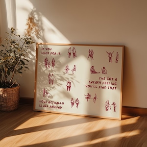 May include: A framed art print with a cream background and a wooden frame. The print features red illustrations of people and text that reads "If you look for it," "Love actually is all around," and "I've got a sneaky feeling you'll find that."