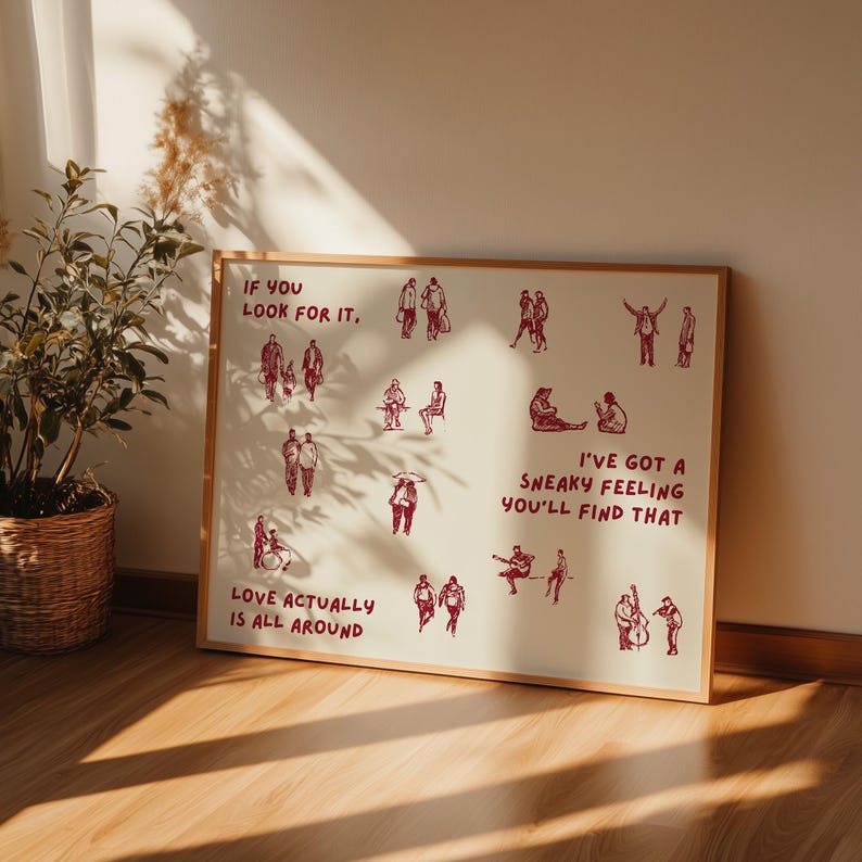 May include: A framed art print with a cream background and a wooden frame. The print features red illustrations of people and text that reads "If you look for it," "Love actually is all around," and "I've got a sneaky feeling you'll find that."