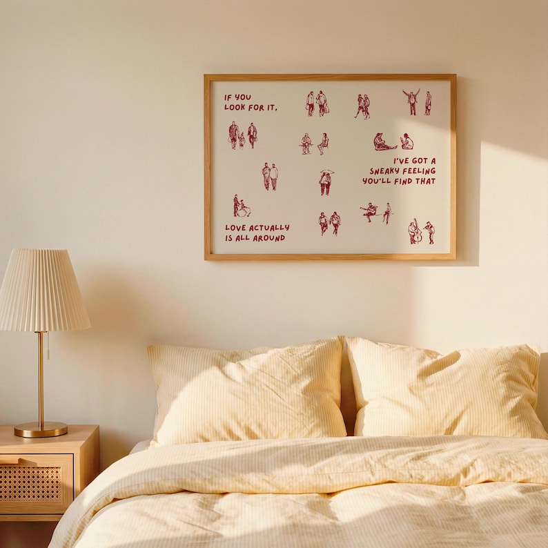 May include: A framed art print with a light wood frame. The print features red illustrations of people and text that reads "IF YOU LOOK FOR IT," "LOVE ACTUALLY IS ALL AROUND," and "I'VE GOT A SNEAKY FEELING YOU'LL FIND THAT."