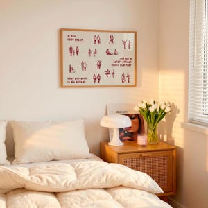 May include: A framed print with the text "IF YOU LOOK FOR IT, LOVE ACTUALLY IS ALL AROUND, I'VE GOT A SNEAKY FEELING YOU'LL FIND THAT" and illustrations of people. A white lamp, a vase of white tulips, and a wooden nightstand are also visible.
