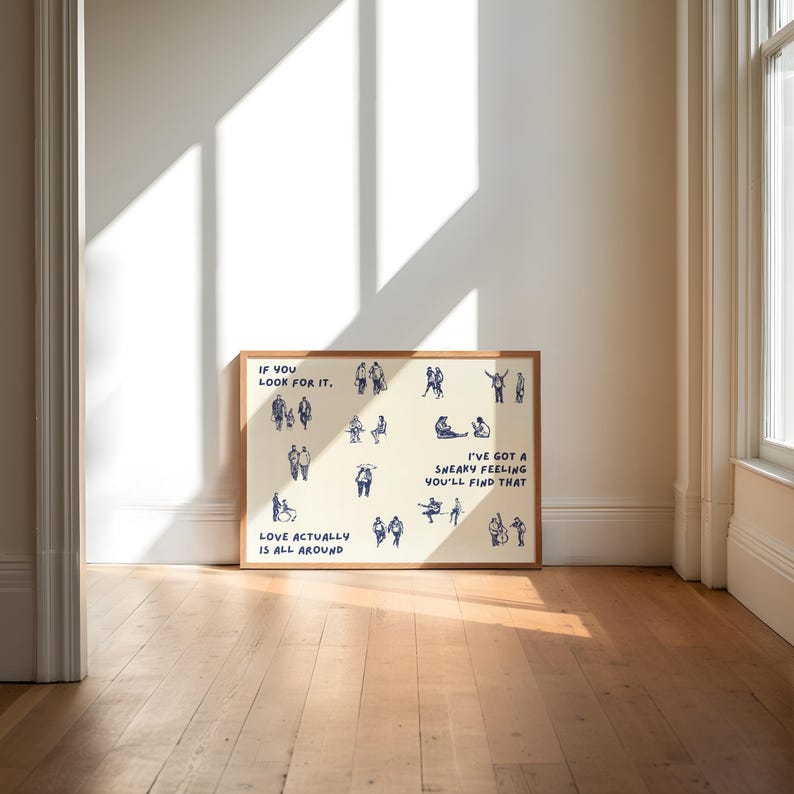 May include: A framed art print with a cream-colored background and a wooden frame. The print features blue line drawings of people in various poses, with text that reads "IF YOU LOOK FOR IT," "LOVE ACTUALLY IS ALL AROUND," and "I'VE GOT A SNEAKY FEELING YOU'LL FIND THAT."