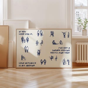 May include: A framed art print with a beige background and a wooden frame. The print features blue ink illustrations of people in various scenes, with text that reads "If you look for it," "Love actually is all around," and "I've got a sneaky feeling you'll find that."