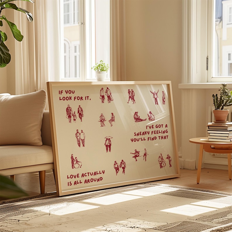 May include: A framed art print with a light beige background and red illustrations of people in various poses. The text "IF YOU LOOK FOR IT," "LOVE ACTUALLY IS ALL AROUND," and "I'VE GOT A SNEAKY FEELING YOU'LL FIND THAT" are also in red.