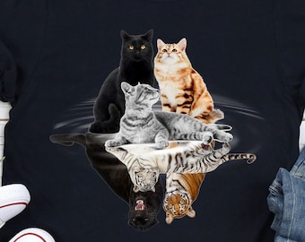 May include: A black t-shirt with a graphic of four cats and their reflections in water. The cats are a black cat, a gray tabby, a brown tabby, and a tiger. The graphic is in a circular shape.