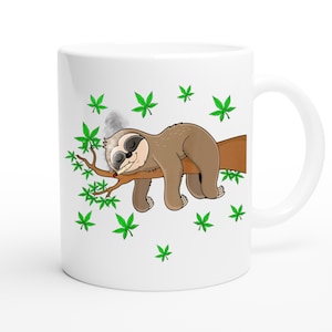 May include: White ceramic mug featuring a cartoon illustration of a sloth sleeping on a branch with green cannabis leaves and smoke coming from its mouth.