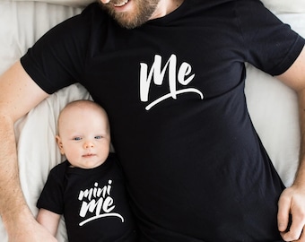 May include: A father and child wearing matching black t-shirts. The father's shirt says "Me" and the child's shirt says "mini me".