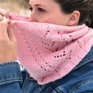 Könnte beinhalten: Ein rosa gestrickter Schal mit einem zarten Spitzenmuster. Der Schal wird von einer Person mit braunen Haaren getragen und bedeckt teilweise ihr Gesicht.