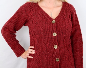 May include: A red cable knit cardigan with a v-neck and button closure. The cardigan has a textured pattern and is made of a soft, warm material.