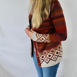 May include: A woman wearing a long-sleeved, red, white, and brown striped cardigan with a geometric pattern on the cuffs and hem. The cardigan is buttoned up and the woman is wearing blue jeans.