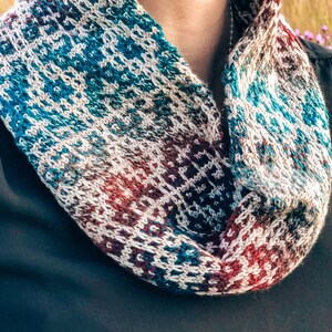 May include: A knitted cowl with a geometric pattern in shades of blue, white, red, and brown.