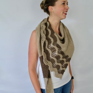 May include: A woman wearing a brown and beige knitted shawl with a lacy pattern. The shawl is draped around her neck and shoulders.