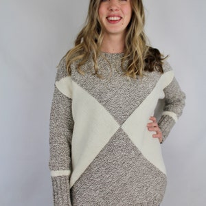 Könnte beinhalten: Ein brauner und weißer Strickpullover mit geometrischem Muster. Der Pullover hat eine lockere Passform und lange Ärmel.