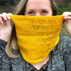 May include: A woman is holding a yellow knitted scarf in front of her face. The scarf has a lacy pattern and is made with a soft yarn.