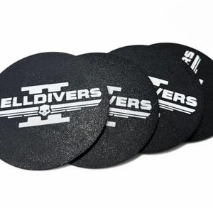 May include: Five black round coasters with a white graphic of a skull and wings with the text "HELLDIVERS II" on one coaster and "IVERS" on the other coasters.
