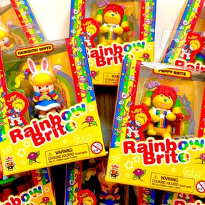 May include: A collection of Rainbow Brite character toys packaged in colorful boxes with the Rainbow Brite logo. The boxes feature a variety of characters, including a bunny, a puppy, and a bear. Each box has a warning label about choking hazards for children under 3 years old.