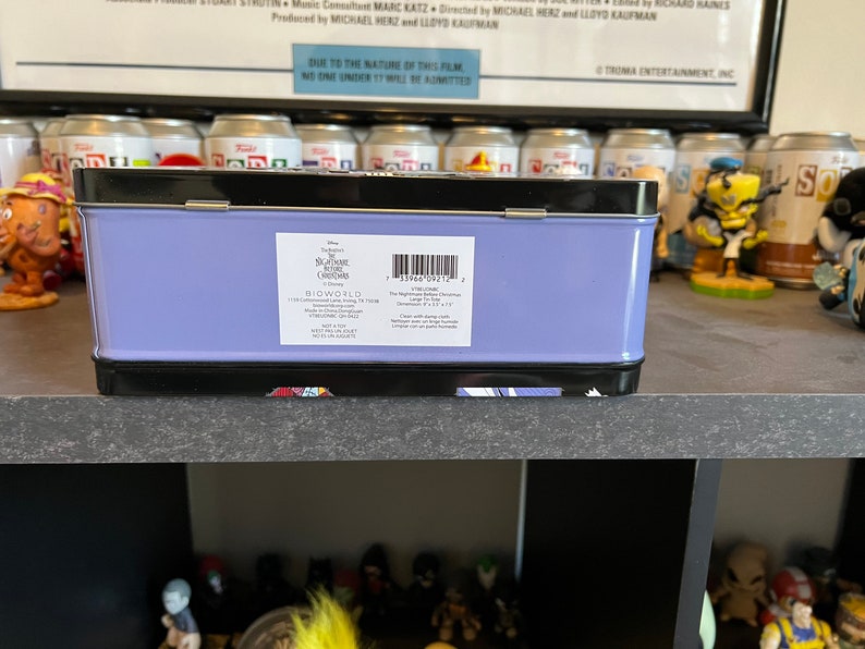 May include: A purple metal lunchbox with a black trim. The front of the box has a white label with the text "Disney's Nightmare Before Christmas" and "Bioworld".