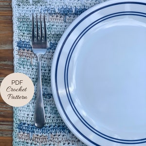 May include: A crocheted placemat in shades of blue, green, and beige with a white plate and silver fork on top. The text "PDF Crochet Pattern" is on a brown circle.