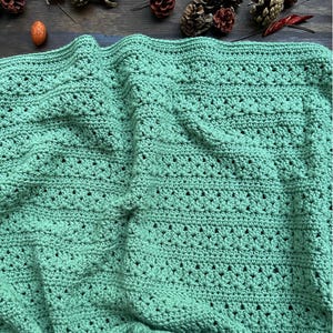 May include: A close-up of a handmade, mint green crochet blanket. The blanket features a textured stitch pattern with small holes throughout. The words "DIGITAL CROCHET PATTERN by Measured and Stitched" are printed vertically on the left side.