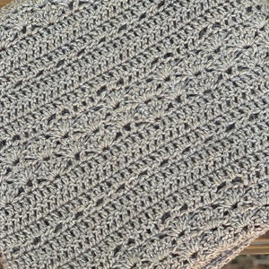 May include: Close-up of a crocheted item in shades of grey. The handmade piece features a detailed, openwork pattern with a textured appearance. The yarn appears to be a blend of light and dark grey, creating a subtle visual depth.