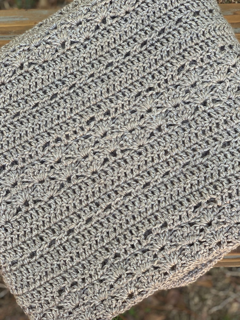 May include: Close-up of a crocheted item in shades of grey. The handmade piece features a detailed, openwork pattern with a textured appearance. The yarn appears to be a blend of light and dark grey, creating a subtle visual depth.
