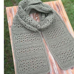 May include: An olive green crocheted scarf featuring alternating rows of solid stitches and openwork patterns. The text DIGITAL CROCHET PATTERN by Measured and Stitched is printed vertically on the left side of the image.