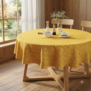 Könnte beinhalten: Eine runde gelbe Tischdecke mit einem weißen geometrischen Dreiecksmuster auf einem Holztisch. Der Tisch ist mit einer weißen Schale, einer kleinen weißen Tasse auf einer Untertasse, einer Glasvase mit weißen Blumen und zwei Holzstreuern gedeckt.