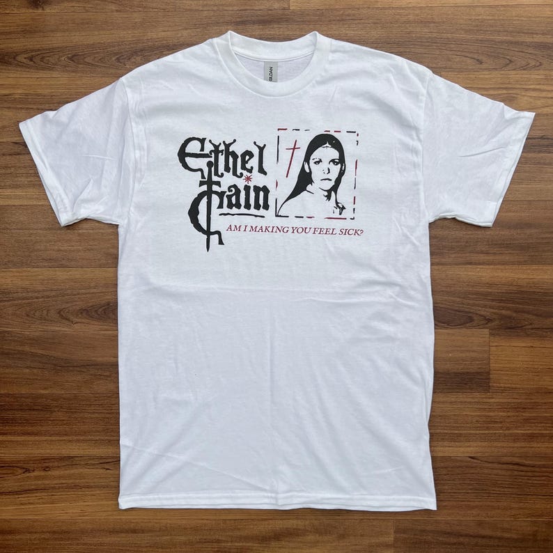 May include: White t-shirt featuring a black graphic with the text "Ethel Cain" and a portrait of a woman. Below the graphic is the text "AM I MAKING YOU FEEL SICK?". The shirt is made of a soft, comfortable material.