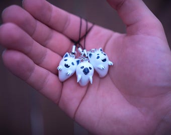 May include: Four white ghost-shaped charms with black eyes and mouths, hanging from black strings. The charms are held in a hand.