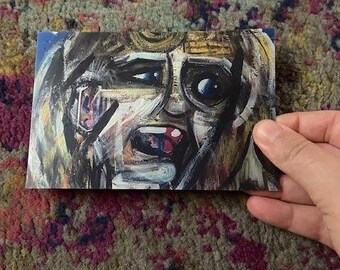 May include: A rectangular art print featuring an abstract portrait with a distressed, expressive face. The artwork uses a palette of blues, browns, and whites, with bold brushstrokes and visible texture. The subject's mouth is open, and the eyes are wide.