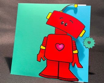 Puede incluir: Una tarjeta turquesa con un robot rojo sosteniendo un corazón. El robot tiene una antena amarilla y detalles amarillos en su cuerpo. La tarjeta tiene una pequeña pegatina en forma de corazón en el lado derecho.