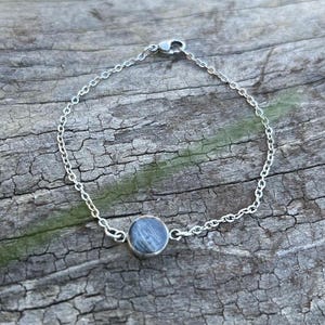Peut inclure: Un bracelet en argent avec une petite pierre bleue ronde sertie dans une lunette en argent. La chaîne du bracelet est délicate et possède un fermoir mousqueton. La pierre mesure environ 1,3 cm de diamètre.