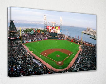 May include: An aerial view of a baseball stadium with a green field and a large scoreboard. The stadium is surrounded by a large crowd of people. The stadium is located on a waterfront with a body of water and a city skyline in the background.