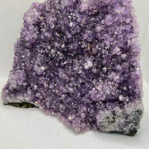 May include: A large amethyst crystal cluster with a purple and white color. The crystal is rough and has a natural, raw look.